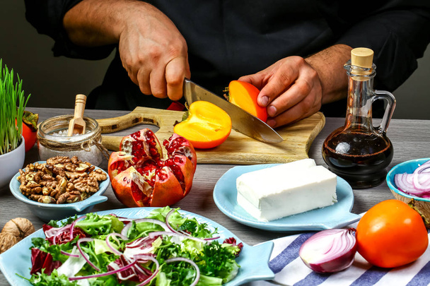 Шеф-повар готовит вкусный салат хурма с рукколой, орехами, сыром фета, фитнес-пищей. Сверхтовары. - Фото, изображение