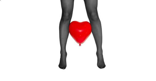 piernas de mujer en los dedos de los pies en medias negras con el corazón rojo globo entre sobre fondo blanco
 - Foto, Imagen