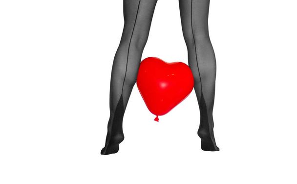 γυναίκα τα πόδια από το πίσω μέρος σε μαύρο καλσόν με κόκκινη καρδιά baloon ανάμεσα σε λευκό φόντο - Φωτογραφία, εικόνα