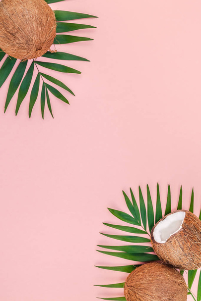 Creative flat lay top view of green tropical palm leaves coconut fruits and coconut oil cosmetics for skin and hair care on pink paper background copy space. Minimal tropical summer beauty spa concept - Valokuva, kuva