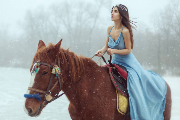 Portrait of a beautiful young brunette riding a horse on a frozen lake. - Photo, Image