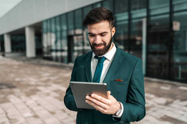 Hombre de negocios sonriente en ropa formal usando tableta mientras está de pie en la azotea
. - Foto, imagen