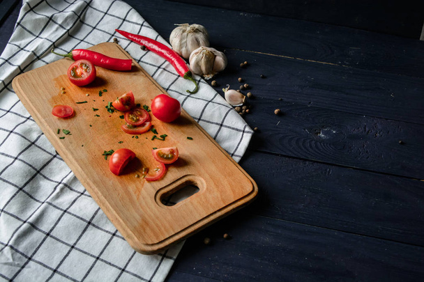 Tomates cereja em uma tábua de madeira com alho, pimenta e tempero em uma toalha de cozinha
 - Foto, Imagem
