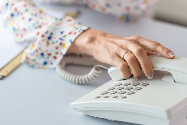 Primer plano del asistente de negocios a punto de recoger un receptor de un teléfono fijo blanco
. - Foto, Imagen