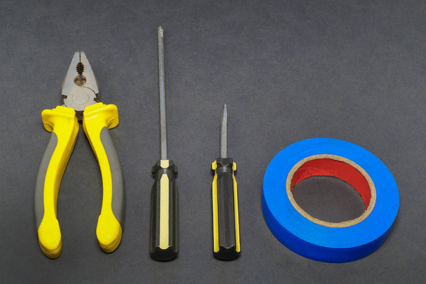 A set of tools on a gray background pliers, screwdriver, insulating tape, saw. - Photo, Image