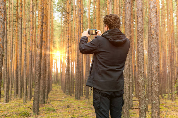 Τουριστικός ταξιδιώτης φωτογραφίζει την ανατολή του ηλίου στο δάσος. - Φωτογραφία, εικόνα