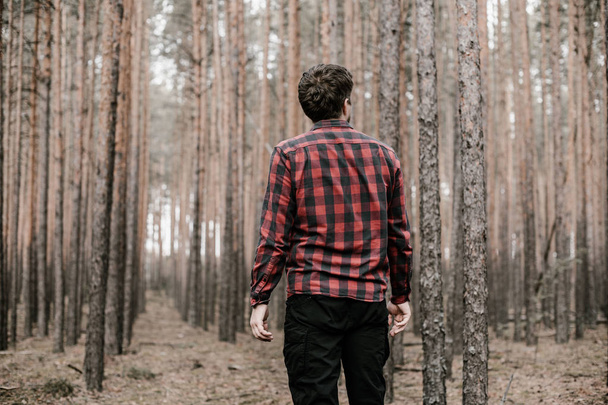 Man in red plaid shirt and black military pants lost in the pine forest. Copy space. Toned - Photo, Image