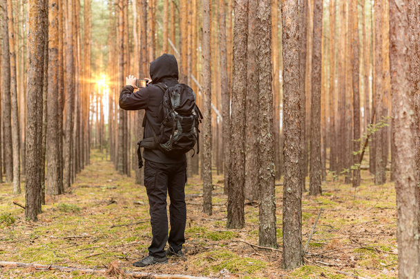 Tourist traveler with backpack taking pictures of sunrise in forest. Copy space - Foto, immagini