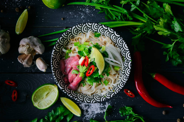 Pho Bo vietnamese soup with noodles, beef, chili pepper, onion,  cilantro and lime on dark black background - Фото, зображення