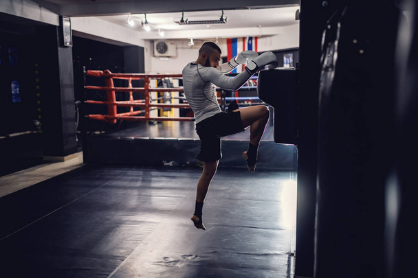 Сильный мощный кавказский боксер с боксерскими перчатками и бинтами на ногах, практикующийся в темном зале
. - Фото, изображение