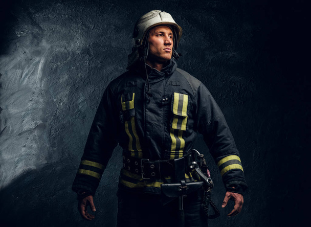 Portret van brandweerman gekleed in uniform en helm zijwaarts op zoek met een zelfverzekerd uiterlijk - Foto, afbeelding