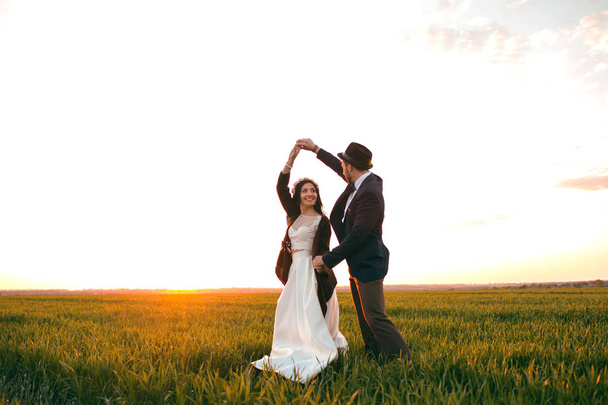 Groom holding bride in dance pose on wedding dayThe groom holds the bride in a dance pose on the wedding day, a young couple dancing at sunset, a stylish groom and a beautiful bride - Fotoğraf, Görsel