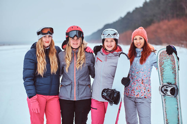 Жінки друзі в спортивному зимовому одязі зі сноубордами і лижами, що стоять разом в обіймах і дивляться на камеру
 - Фото, зображення