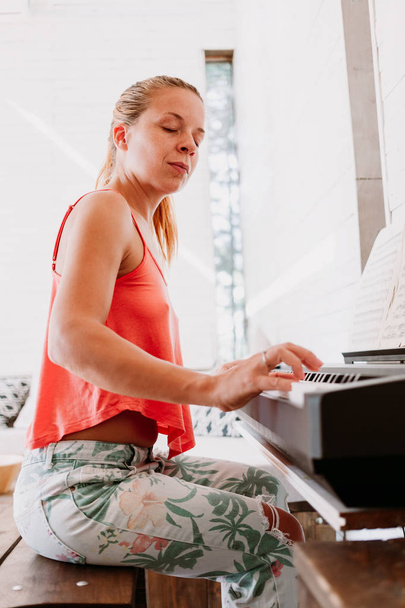 Young woman enjoying playing electric piano at home - 写真・画像