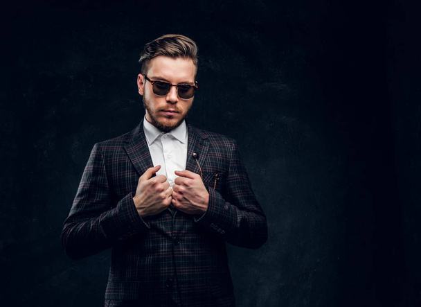 A confident elegantly dressed man in sunglasses against a dark textured wall - Photo, Image