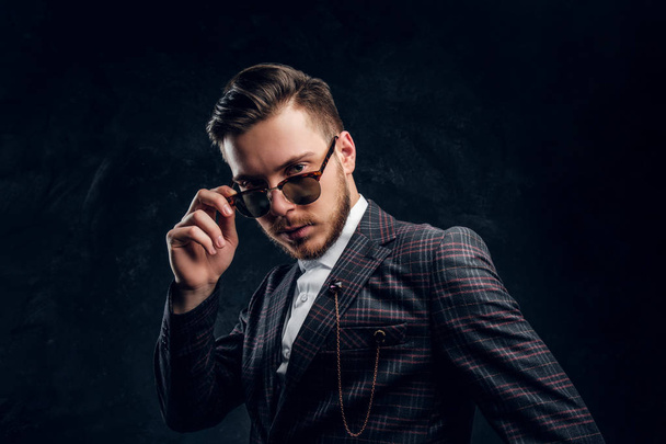 Elegantly dressed young man in sunglasses against a dark textured wall - Foto, imagen