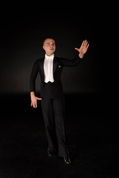 Beautiful dancer performs tango dance, man in black suit and white shirt standing in dance pose on black background - Foto, Imagem