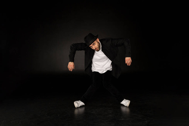 Knappe man, gekleed in een stijlvolle zwarte kleding danst Streetdance - Foto, afbeelding