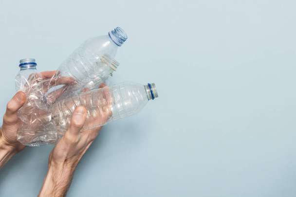 Hand holding empty plastic bottle recycling against a blue background - 写真・画像