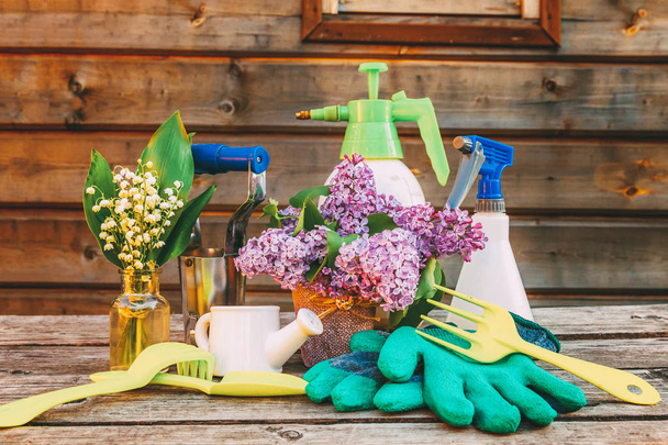 Gardening tools, watering can, shovel, spade, pruner, rake, glove, lilac flowers on wooden table in barn. Spring or summer in garden. Eco nature horticulture hobby concept background - Photo, Image