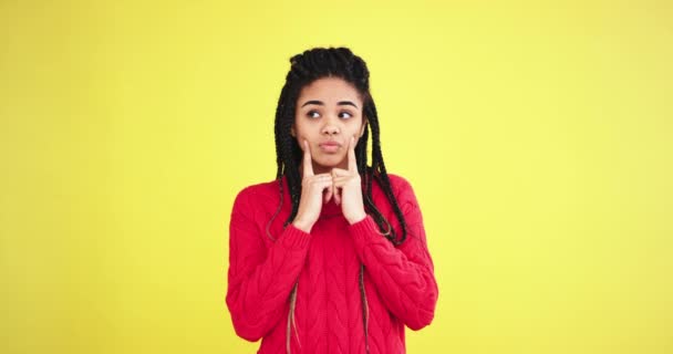 Portrait of a charismatic african lady in a red sweater in the studio with a yellow background wall curiously thinking what decision to take. slow motions - Кадры, видео