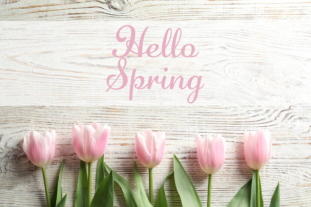 Flat lay composition of beautiful flowers and text Hello Spring on light wooden background - Fotó, kép
