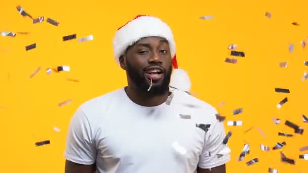 Black man in santa hat winking and showing thumbs up under falling confetti - Filmmaterial, Video
