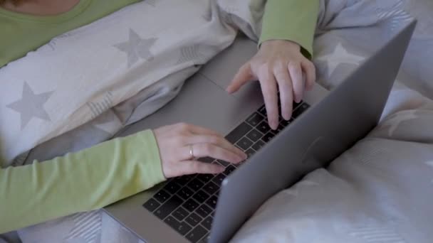 Woman Working on Laptop Computer at Bedroom. Close up Female Hands pressing keys on Laptop Keyboard while relaxing in Bed at morning. Side view. - Video, Çekim