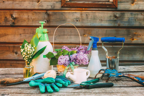 Gardening tools, watering can, shovel, spade, pruner, rake, glove, lilac flowers on wooden table in barn. Spring or summer in garden. Eco nature horticulture hobby concept background - Фото, зображення