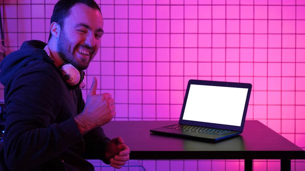 A young cheerful gamer smiling to the camera and looking at laptop. White Display. - Fotografie, Obrázek