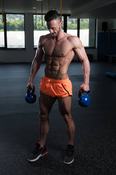 Man Working Out With Kettle Bell In A Dark Gym - Bodybuilder Doing Heavy Weight Exercise With Kettle-bell - Foto, afbeelding
