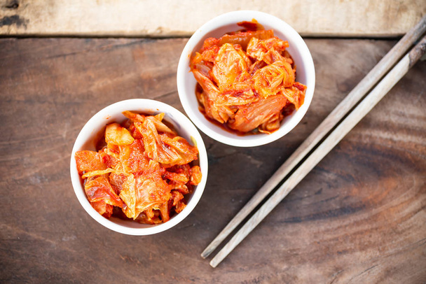 Капуста кимчи в миске с палочками для еды на деревянном столе, корейская еда
 - Фото, изображение
