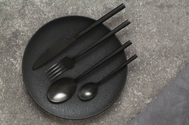 Black plate, cutlery on stone table top view. Table setting. - Φωτογραφία, εικόνα