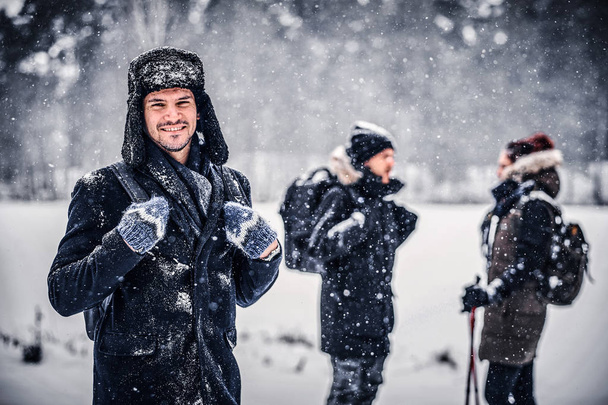Портрет улыбающегося туриста с рюкзаком, гуляющего с друзьями по зимнему лесу
 - Фото, изображение