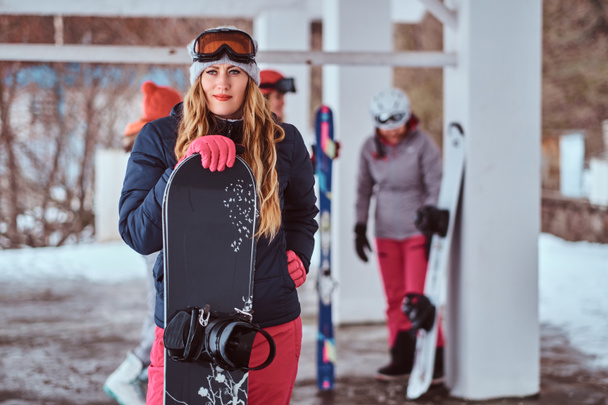 Norwegian woman wearing warm clothes and goggles posing with a snowboard in the winter ski resort - Photo, Image