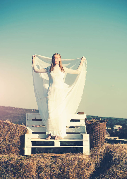 Woman bride in wedding dress on wooden bench. Sensual woman with long blond hair. Albino girl on idyllic landscape, natural beauty. Fashion model on sunny blue sky - Foto, imagen