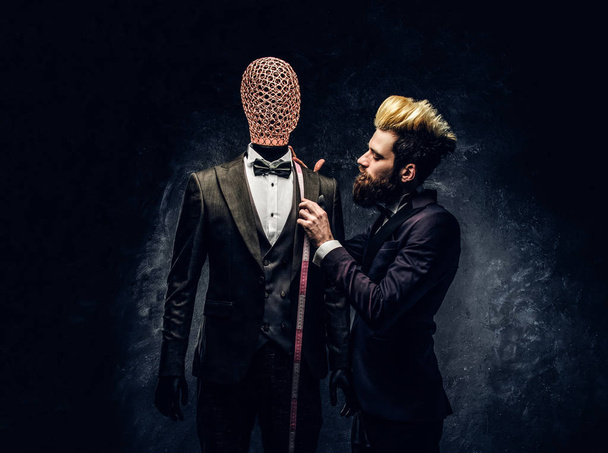 Σχεδιαστής μόδας με εκφραστικό στυλ εργασίας με custom made mens κοστούμι σε ένα σκοτεινό ράφτης στούντιο - Φωτογραφία, εικόνα