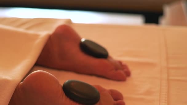 Foot massage with hot stone and spa therapy in luxury resort hotel. Young woman relaxing while stone massage in spa salon. Body relax and skin care concept. Healthy lifestyle. Wellness concept - Video, Çekim