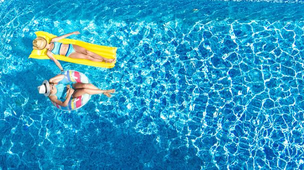 Gyerekek medencében drón kilátás fentről, boldog gyerekek úszni felfújható gyűrű fánk és matrac, aktív lányok szórakozni a vízben családi nyaralás üdülőhelyen - Fotó, kép