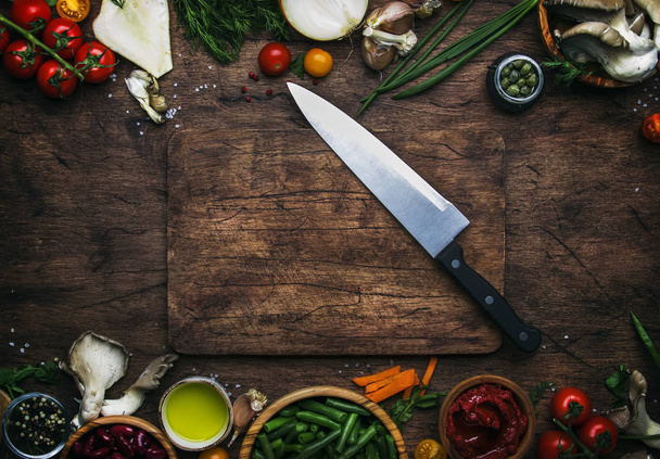 Food cooking background, ingredients for preparation vegan dishes, vegetables, roots, spices, mushrooms and herbs. Big kitchen chef knife. Healthy food concept. Rustic wooden table background, top view - 写真・画像
