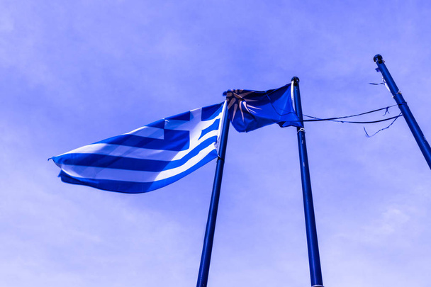 Grieks en blauw gekleurde Macedonische Vergina Sun vlag zwaaien op vlaggenmasten - Foto, afbeelding