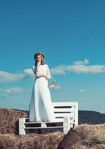 Sensual woman in wreath on long blond hair. Woman bride in wedding dress on wooden bench. Albino girl with flowers, natural beauty. Fashion model at sunny blue sky on vacation - Fotografie, Obrázek