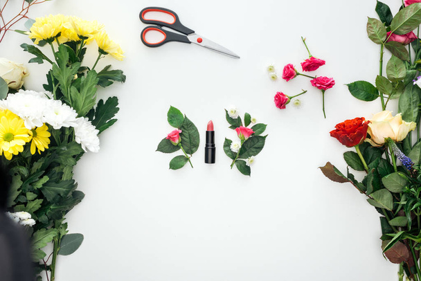 top view of pink rose buds, lipstick and scissors surrounded by flowers on white background - Photo, Image