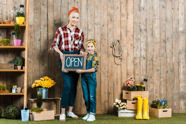 attractive woman holding small chalkboard with open lettering near cute daughter  - Foto, imagen