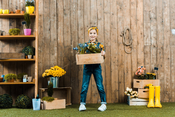 cute kid holding box with plants and standing near wooden fence - Photo, Image