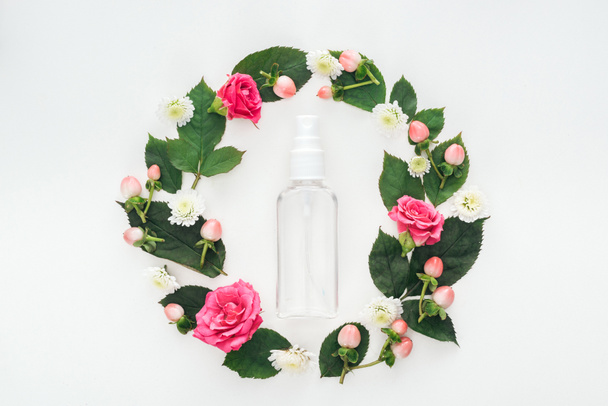 top view of circular composition with green leaves, flowers and empty spray bottle isolated on white - Foto, afbeelding