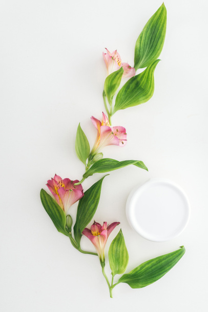 top view of composition with pink flowers, green leaves and beauty cream in bottle on white background - Fotó, kép