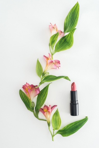 top view of composition with pink flowers, green leaves and lipstick on white background - Fotó, kép