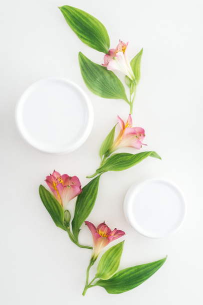 top view of composition with pink alstroemeria flowers, green leaves and beauty cream in bottles on white background - Foto, immagini