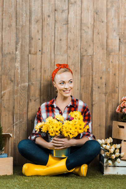 smiling woman sitting with crossed legs and holding flowers in bucket - Foto, immagini
